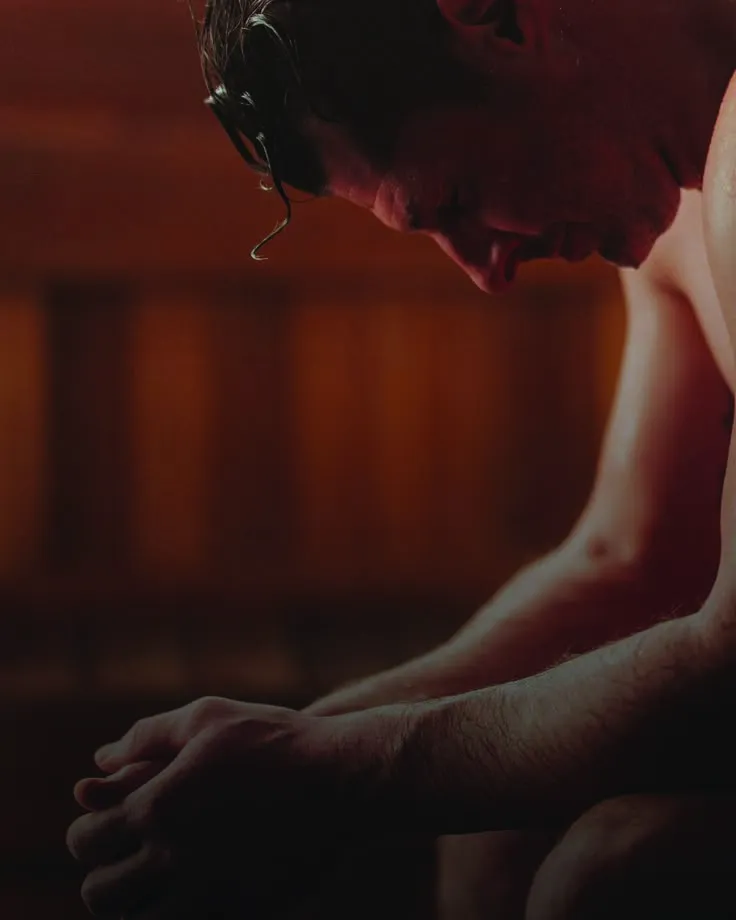 A man resting with his head bowed in a warm, dim sauna